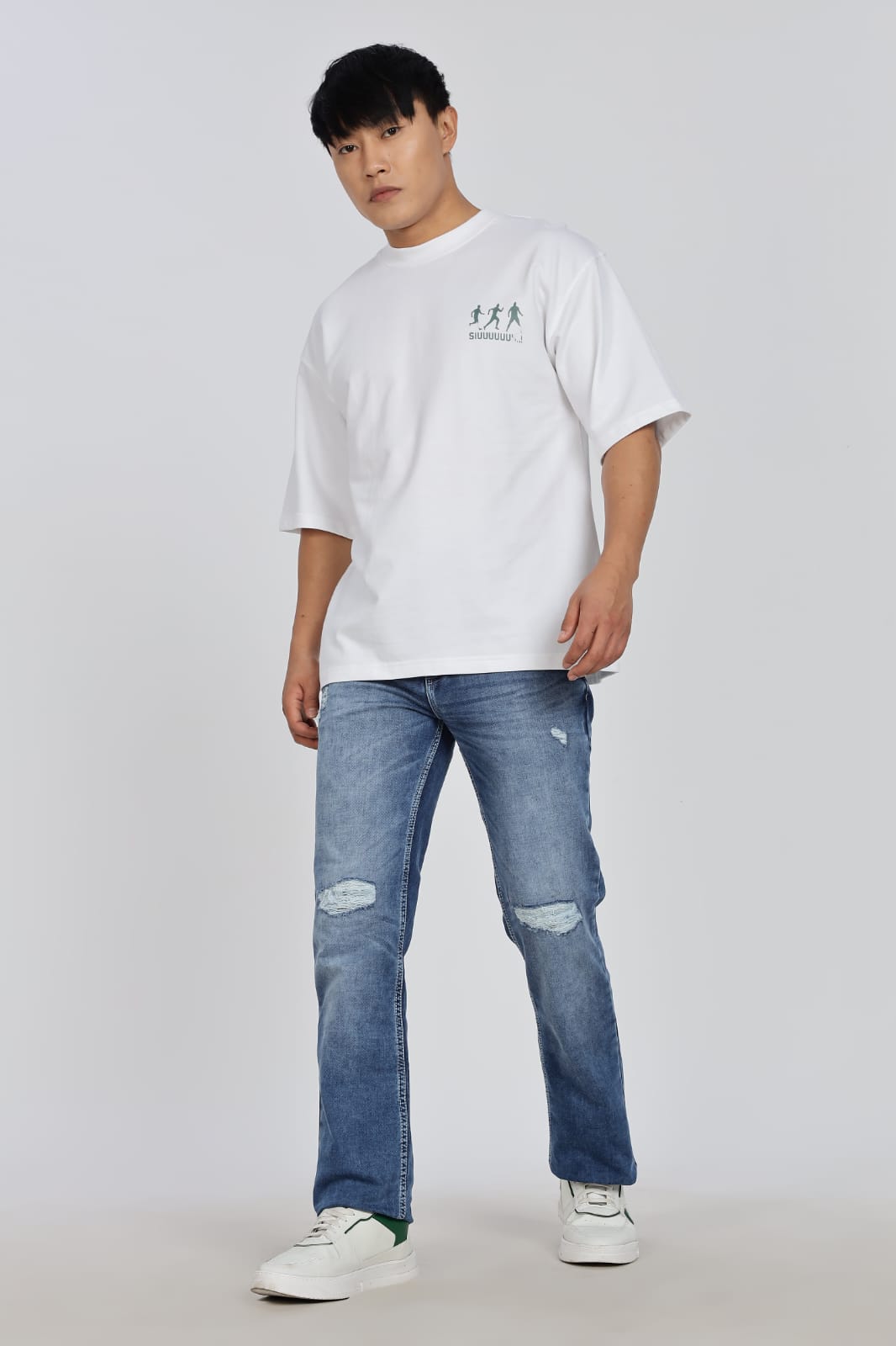 Person wearing a white t-shirt and blue jeans sitting on a white cube.