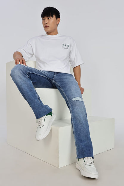 Person wearing a white t-shirt and blue jeans sitting on a white cube.