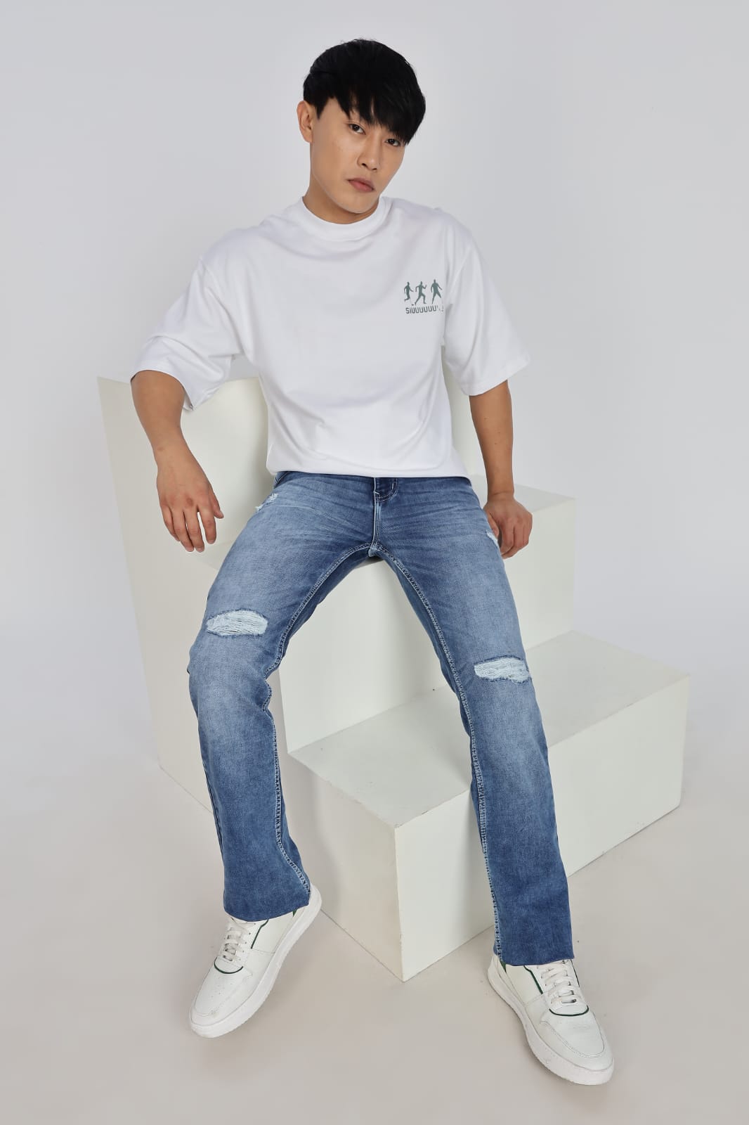 Person wearing a white t-shirt and blue jeans sitting on a white chair against a white background
