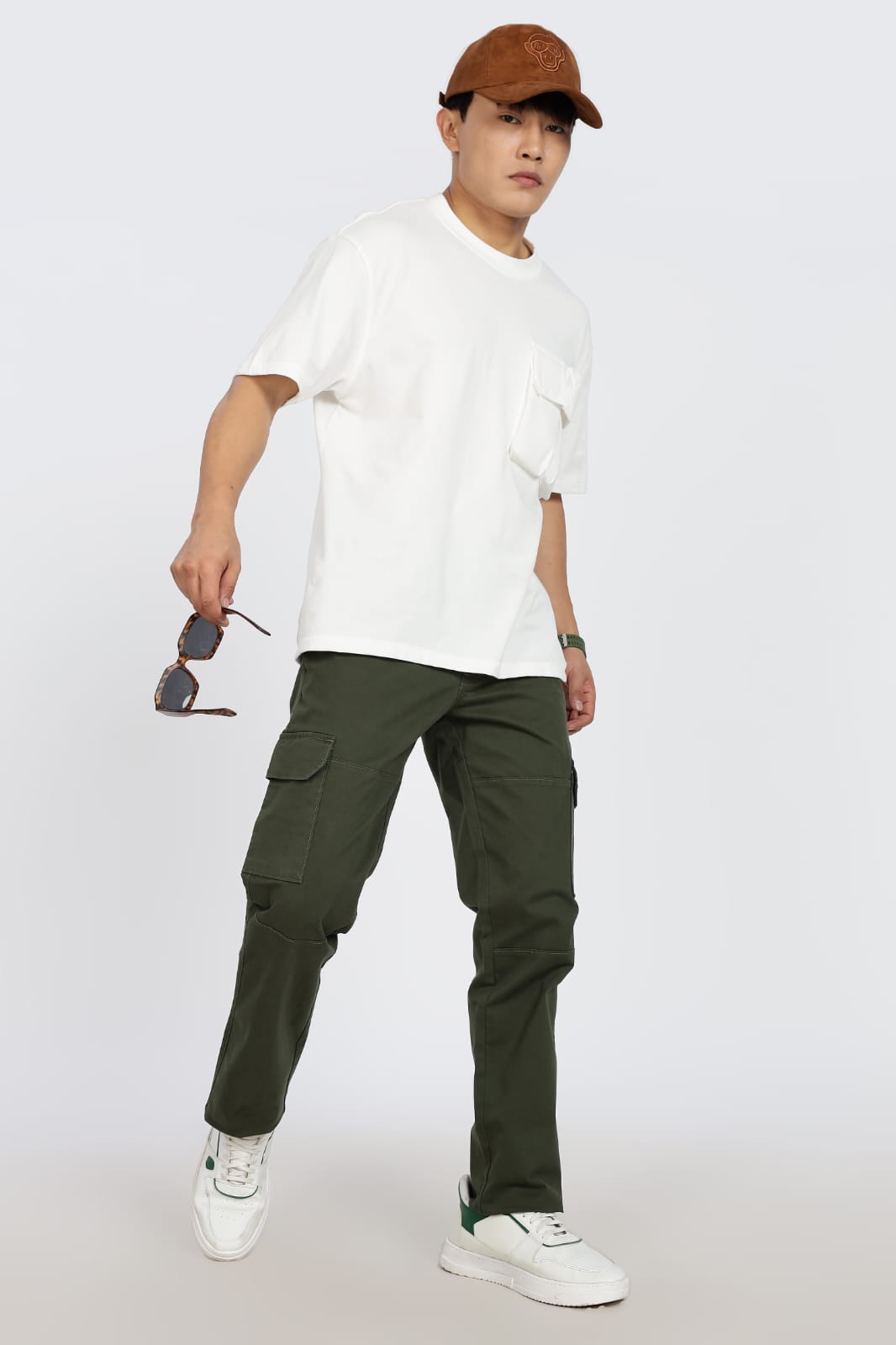 Person wearing a white t-shirt, green cargo pants, and a brown cap on a light gray background