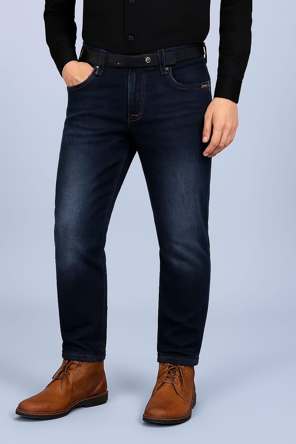 Person wearing dark blue jeans and brown shoes on a light gray background