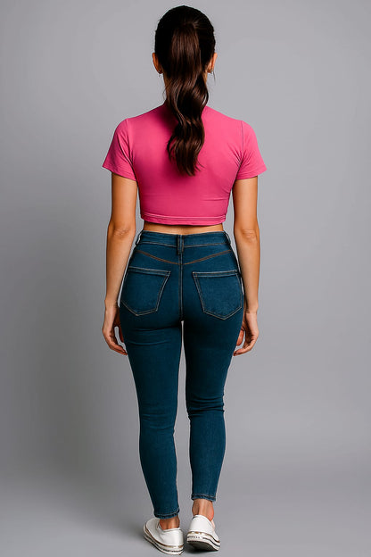 Person wearing a pink crop top and blue jeans on a gray background