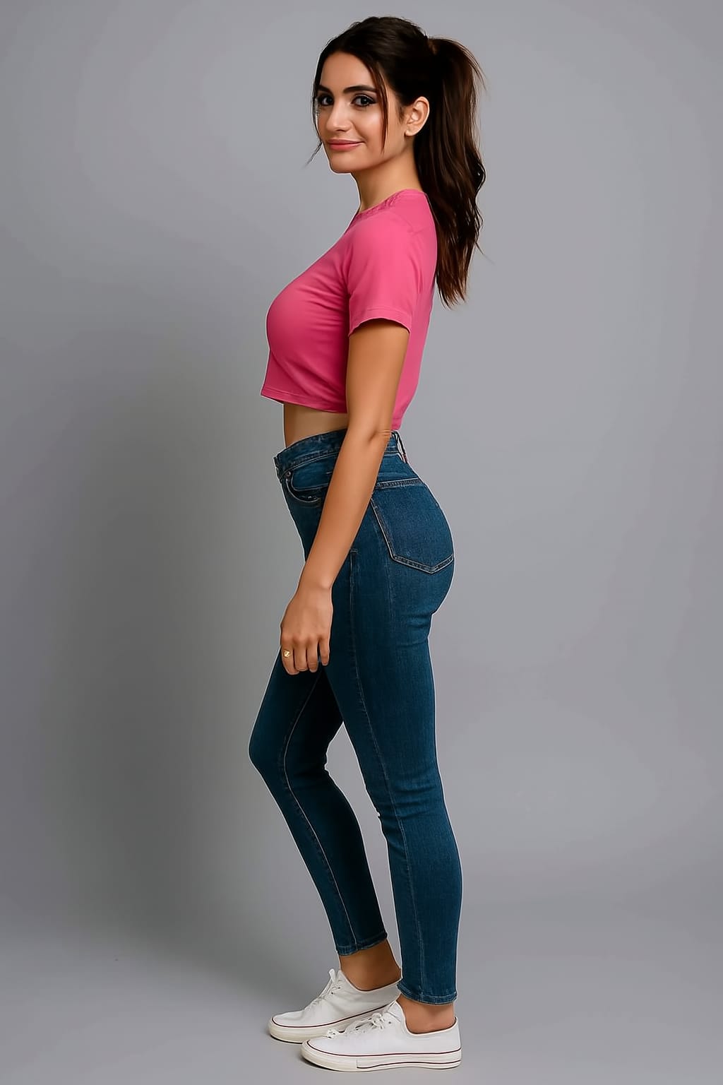 Person wearing a pink crop top and blue jeans on a gray background