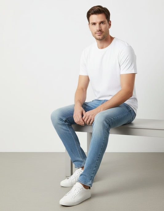 Man sitting on a bench wearing a white t-shirt, blue jeans, and white sneakers.
