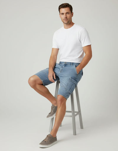 Man sitting on a stool wearing a white t-shirt and blue denim shorts against a plain background