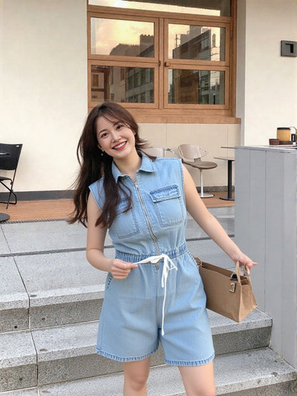 Woman in a denim romper standing outdoors near a building entrance.
