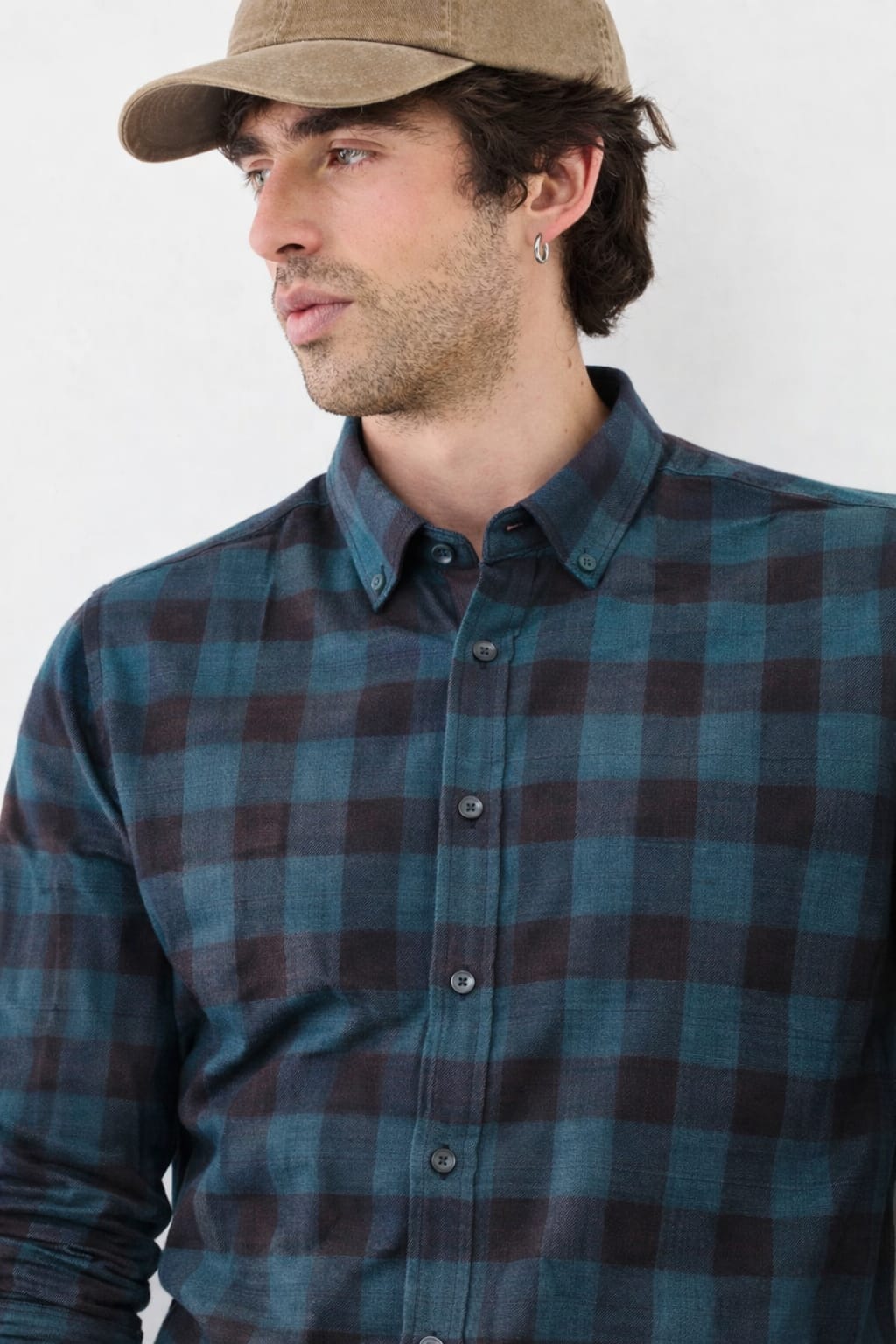 Man wearing a blue plaid shirt and beige cap against a white background