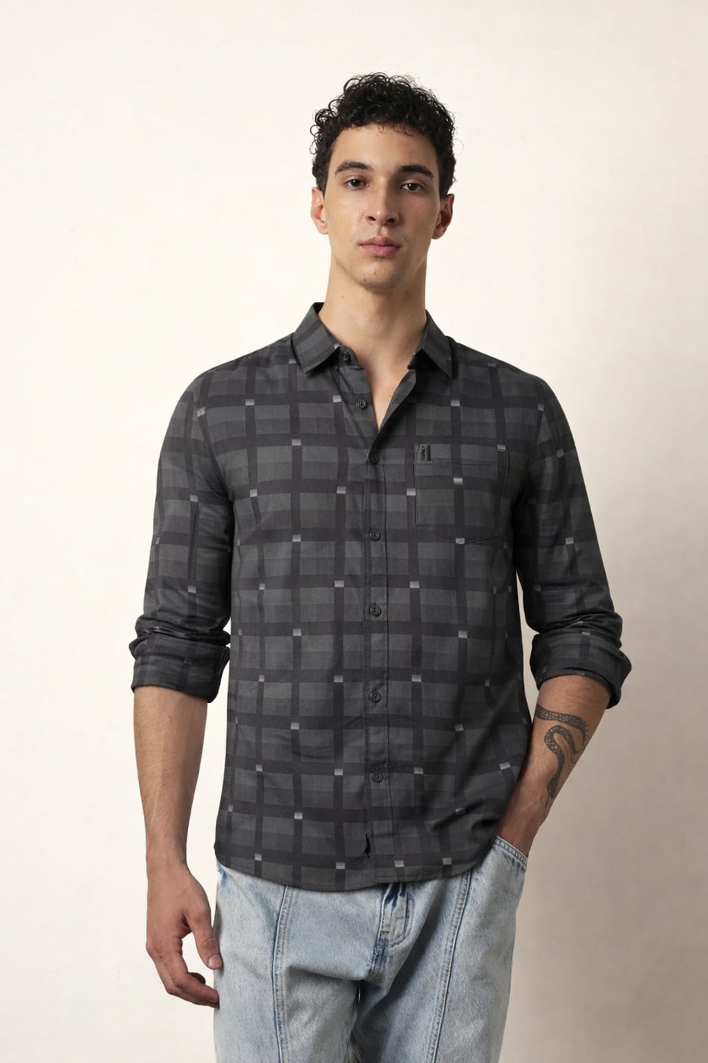 Man wearing a dark plaid shirt and light jeans against a plain background