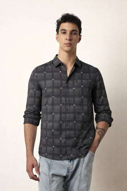 Man wearing a dark plaid shirt and light jeans against a plain background