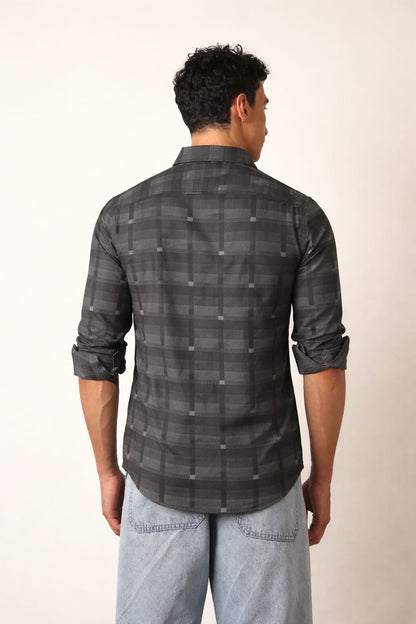 Man wearing a gray plaid shirt and light blue jeans against a white background