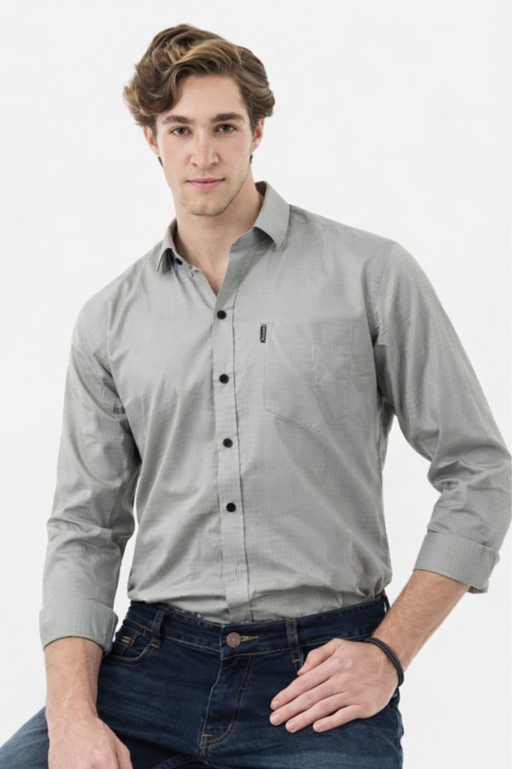 Man wearing a gray button-up shirt and dark jeans on a white background