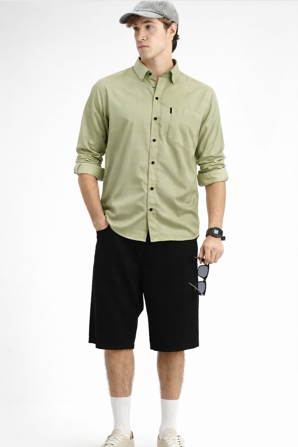 Man wearing a light green button-up shirt, black shorts, and a cap on a white background