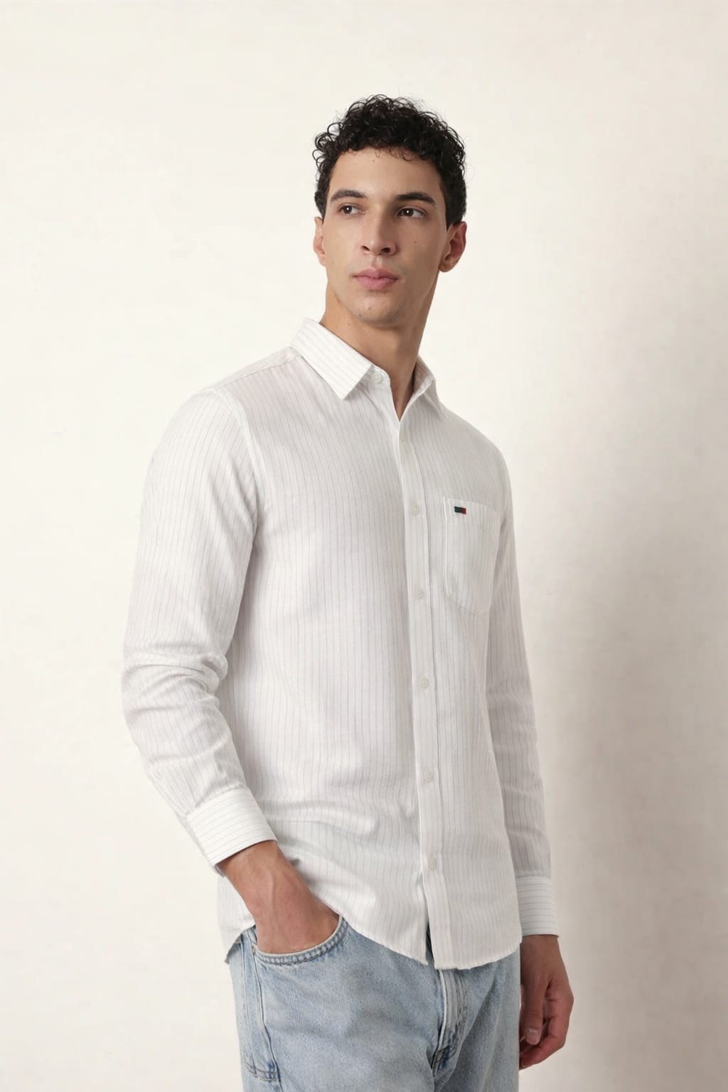 Man wearing a white button-up shirt and light blue jeans against a plain background