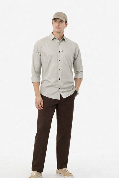 Man wearing a light gray button-up shirt and brown pants on a white background