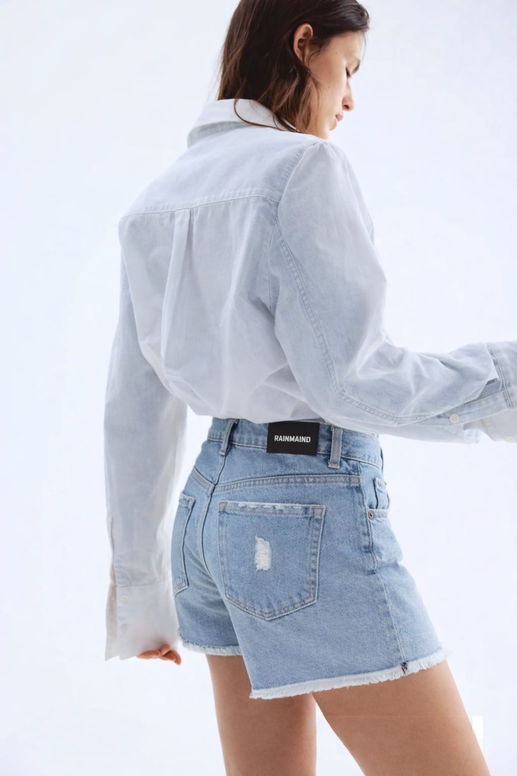 Person wearing a light blue denim shirt and shorts on a white background