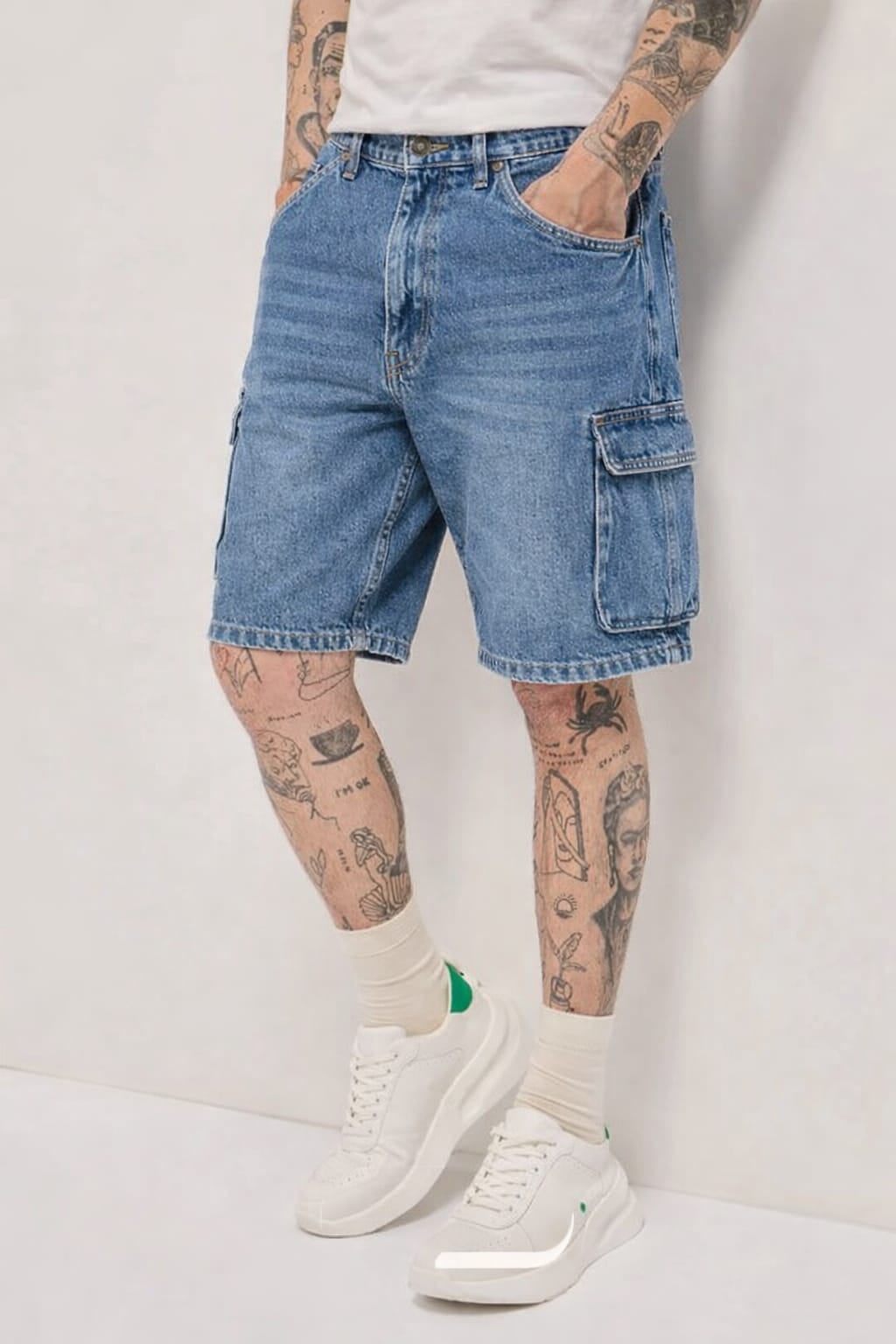 Person wearing blue denim shorts with tattoos on arms and legs against a plain background
