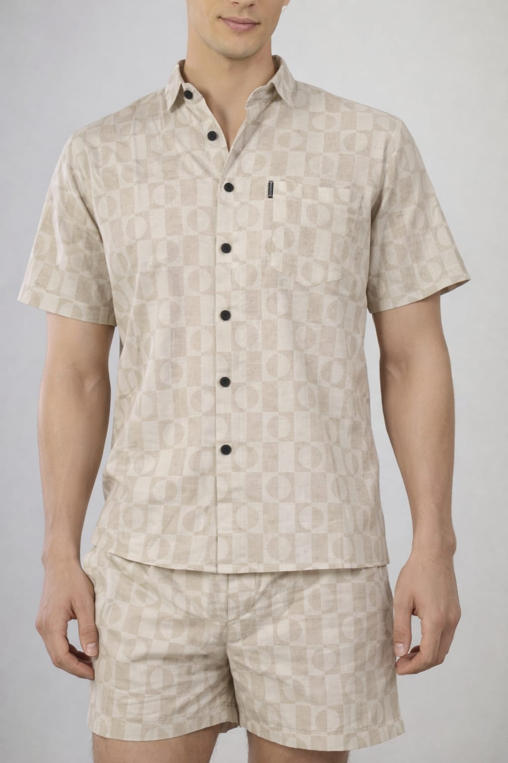 Man wearing a beige patterned shirt and shorts set on a plain background