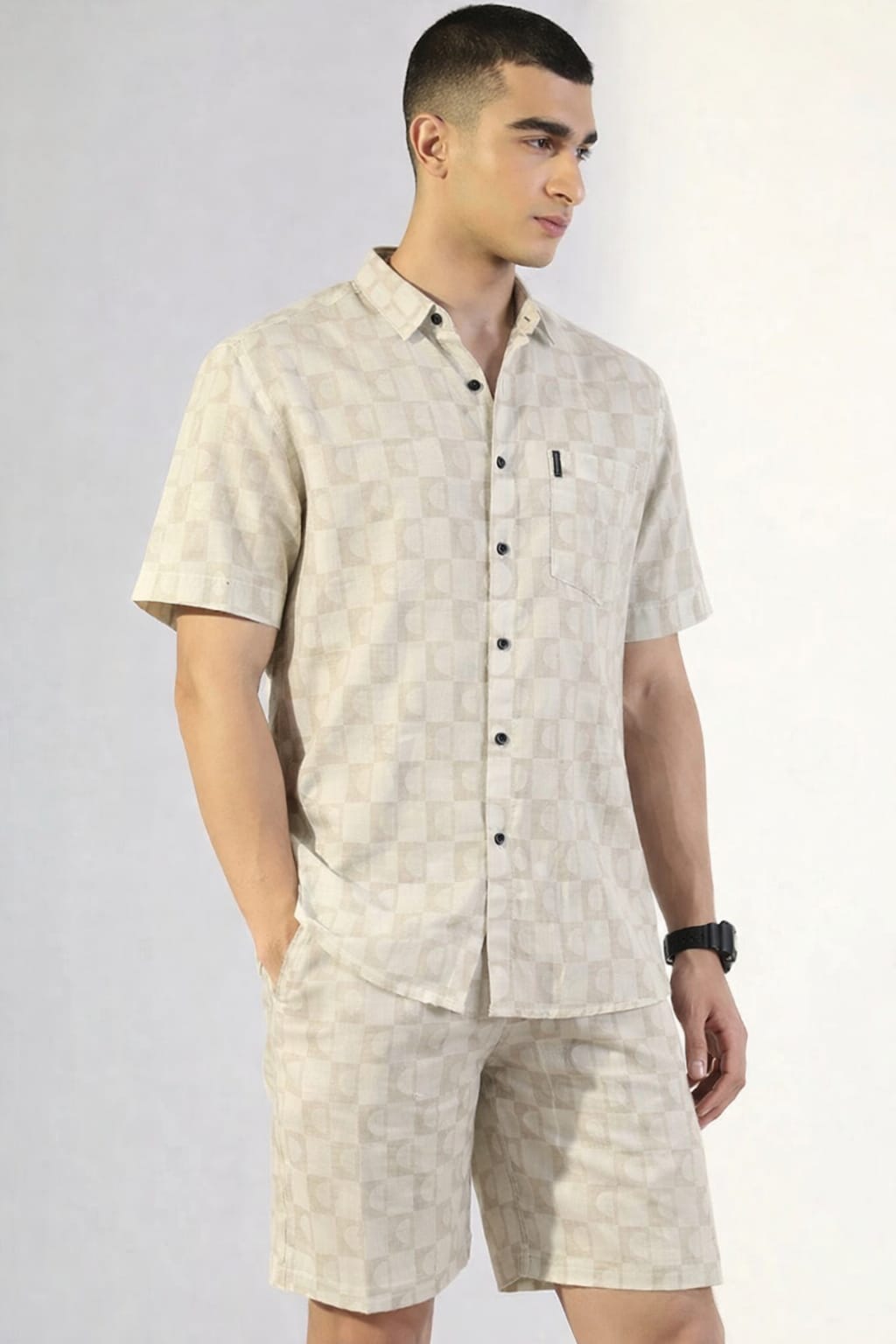 Man wearing a beige patterned shirt and shorts set on a plain background