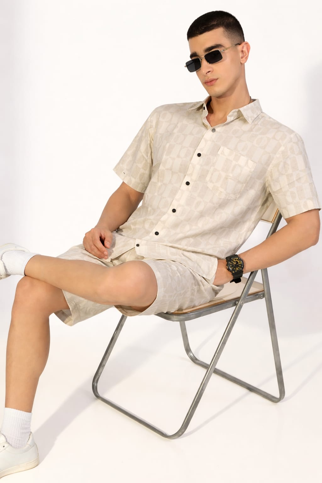 Man sitting on a chair wearing a light-colored shirt and shorts with a white background