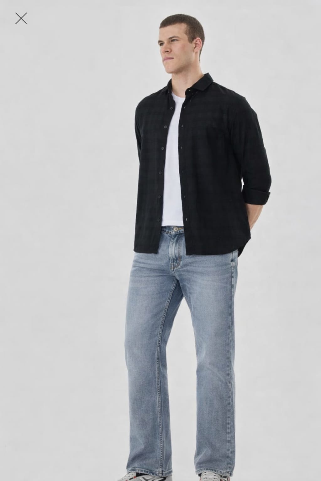 Man wearing a black shirt and light blue jeans on a white background