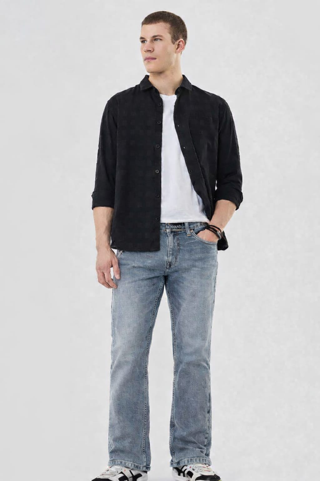Man wearing a black shirt, white t-shirt, and blue jeans on a light gray background