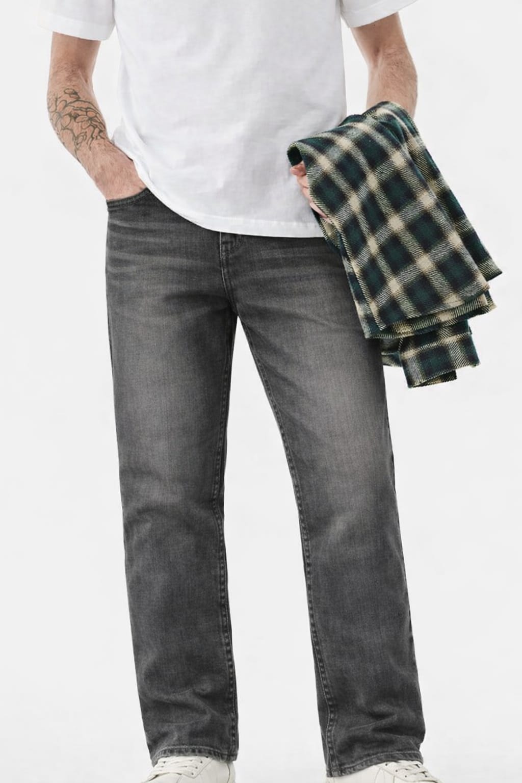 Person wearing gray jeans and a white t-shirt, holding a plaid shirt against a white background