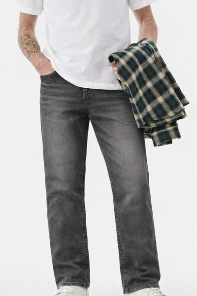 Person wearing gray jeans and a white t-shirt, holding a plaid shirt against a white background