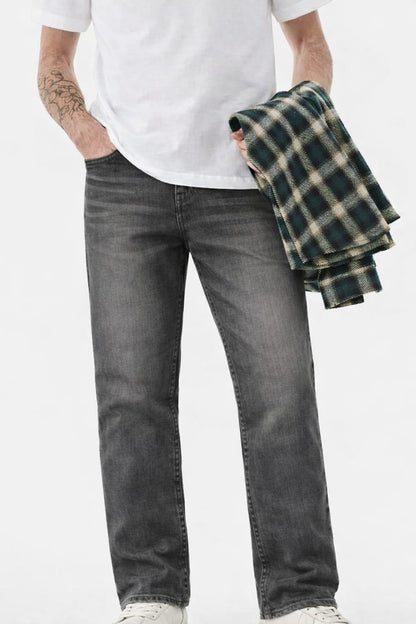 Person wearing gray jeans and a white t-shirt, holding a plaid shirt against a white background