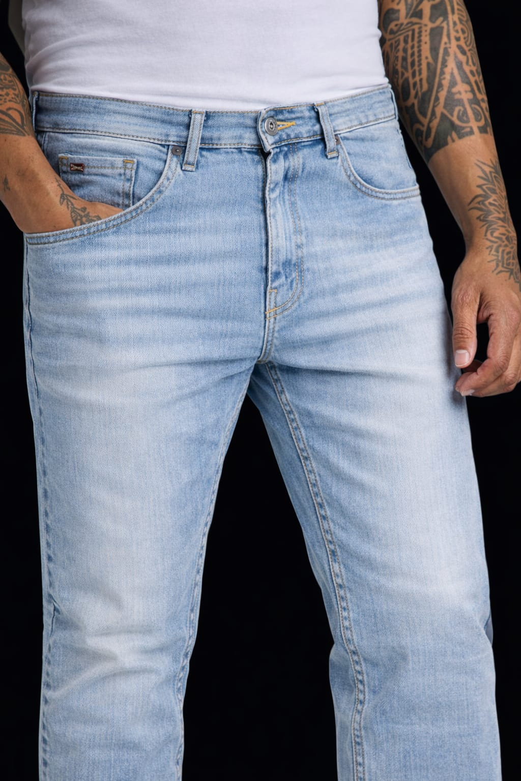 Light blue jeans worn by a person with tattoos on a black background