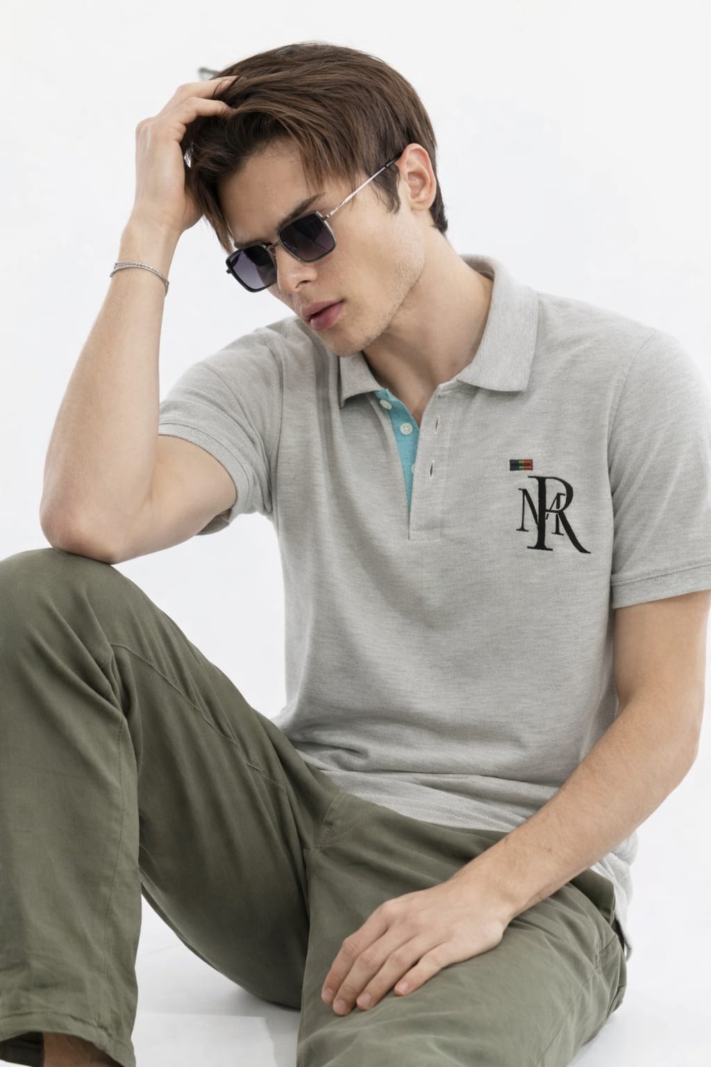 Man wearing a gray polo shirt with a logo, sitting on a white background