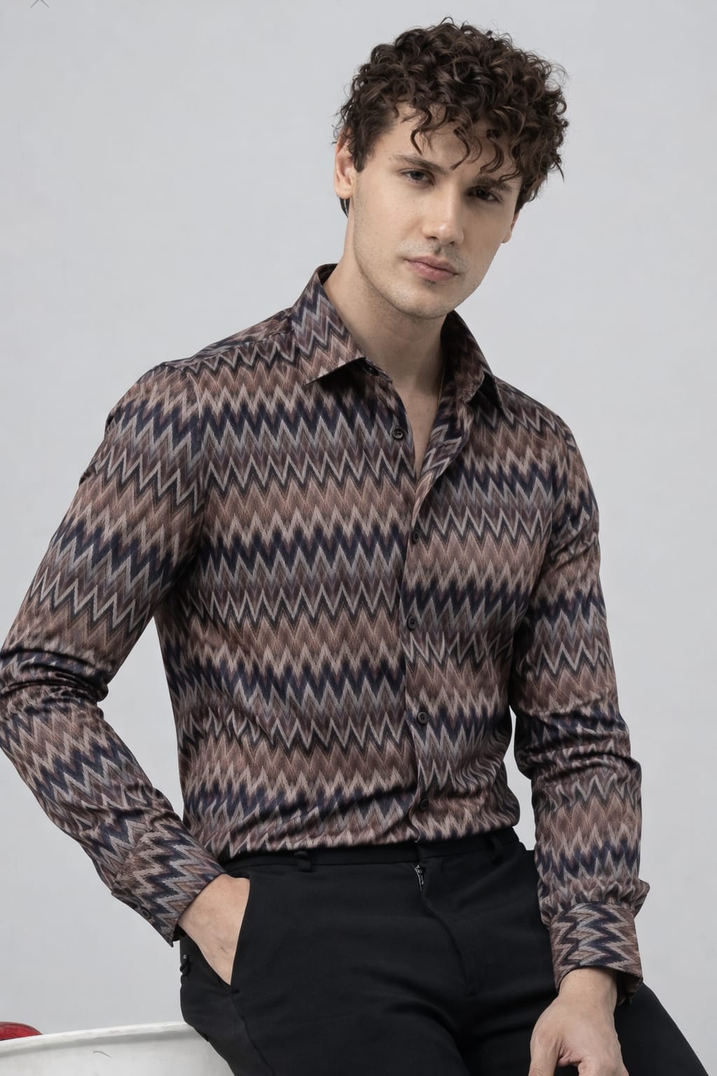 Man wearing a patterned shirt sitting against a plain background