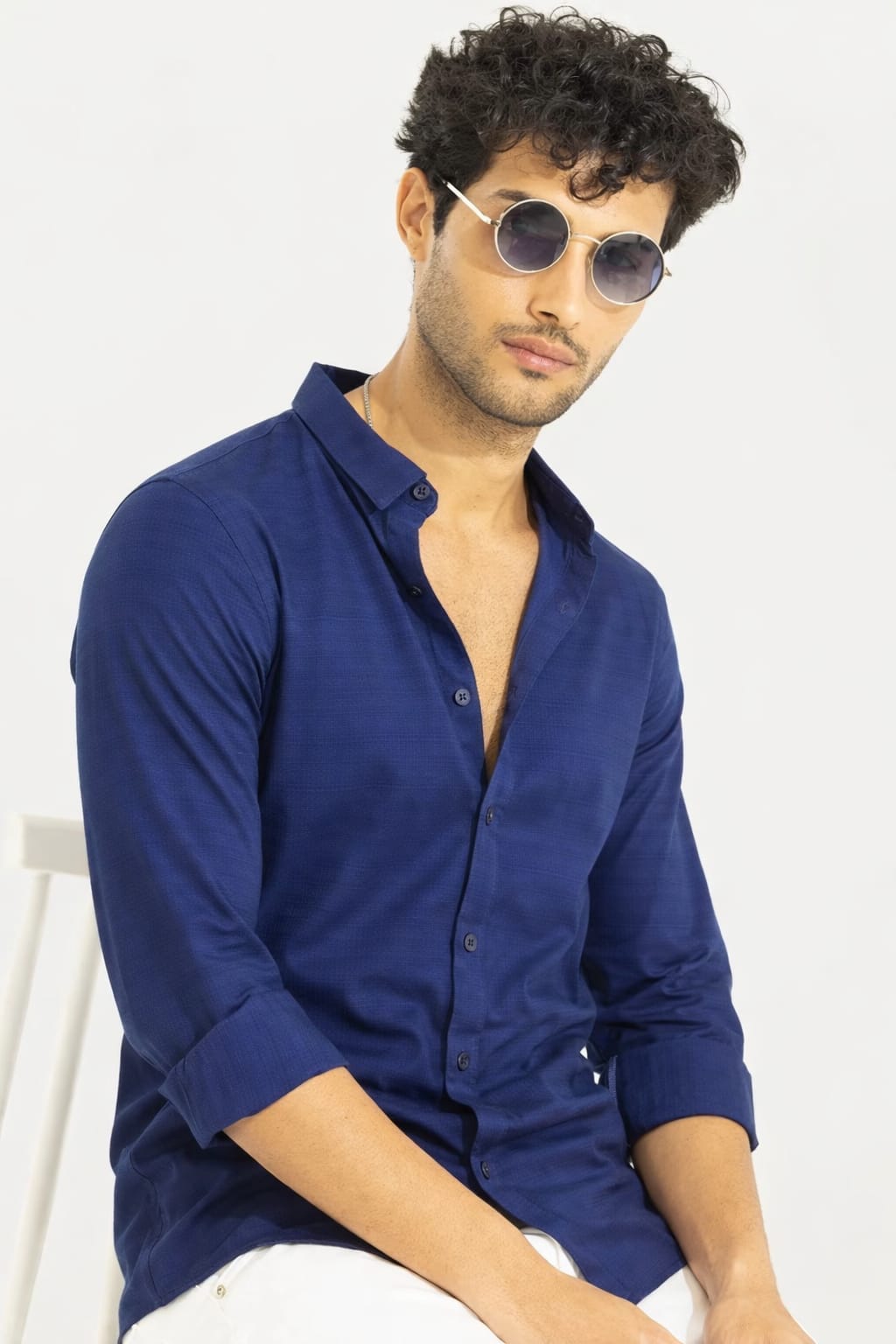 Man wearing a blue shirt and sunglasses on a white background