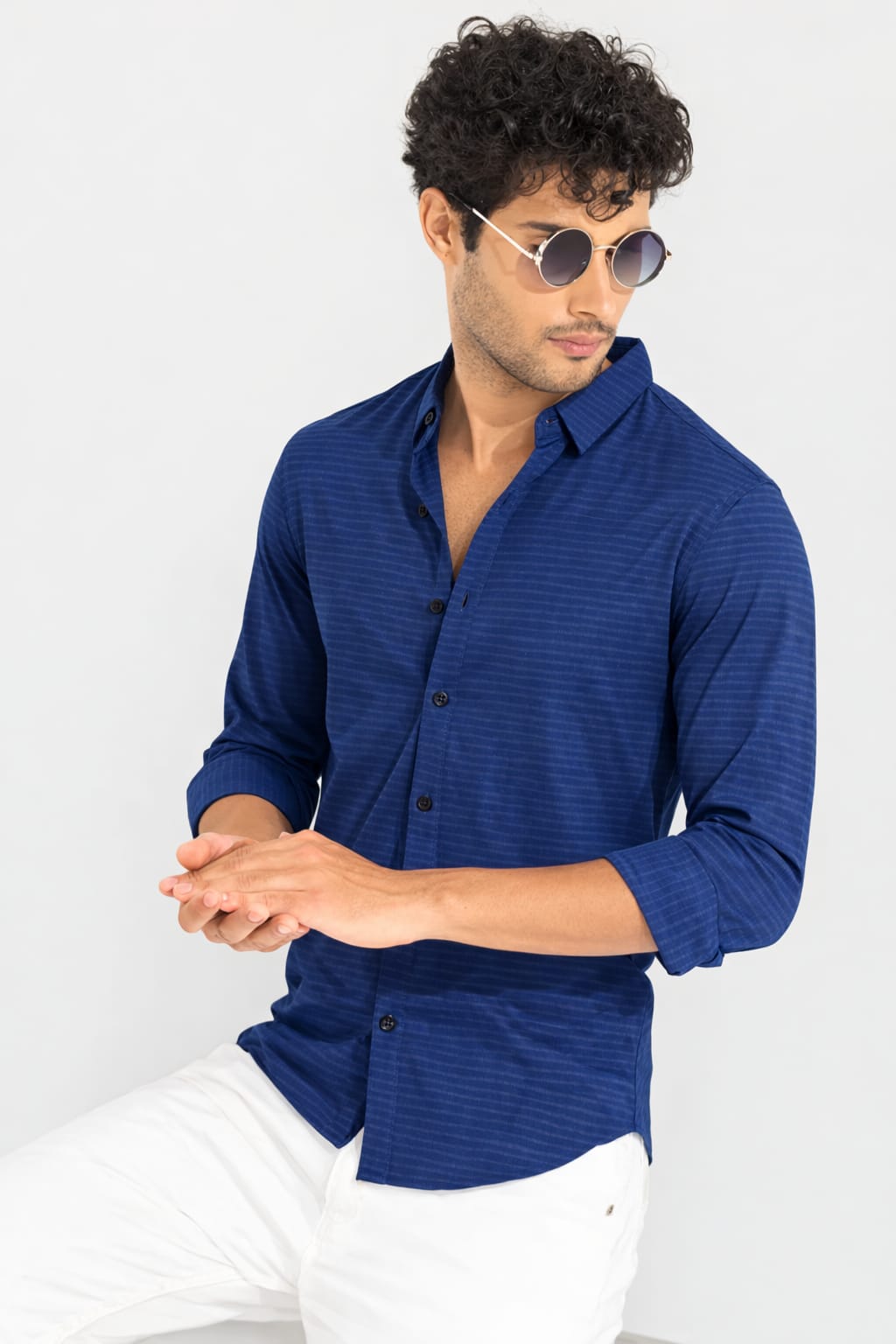 Man wearing a blue shirt and white pants against a light gray background