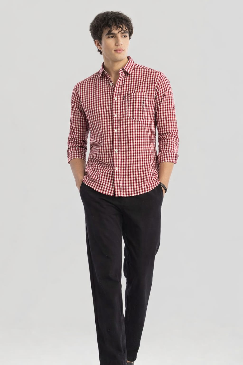 Man wearing a red and white checkered shirt and black pants on a light gray background