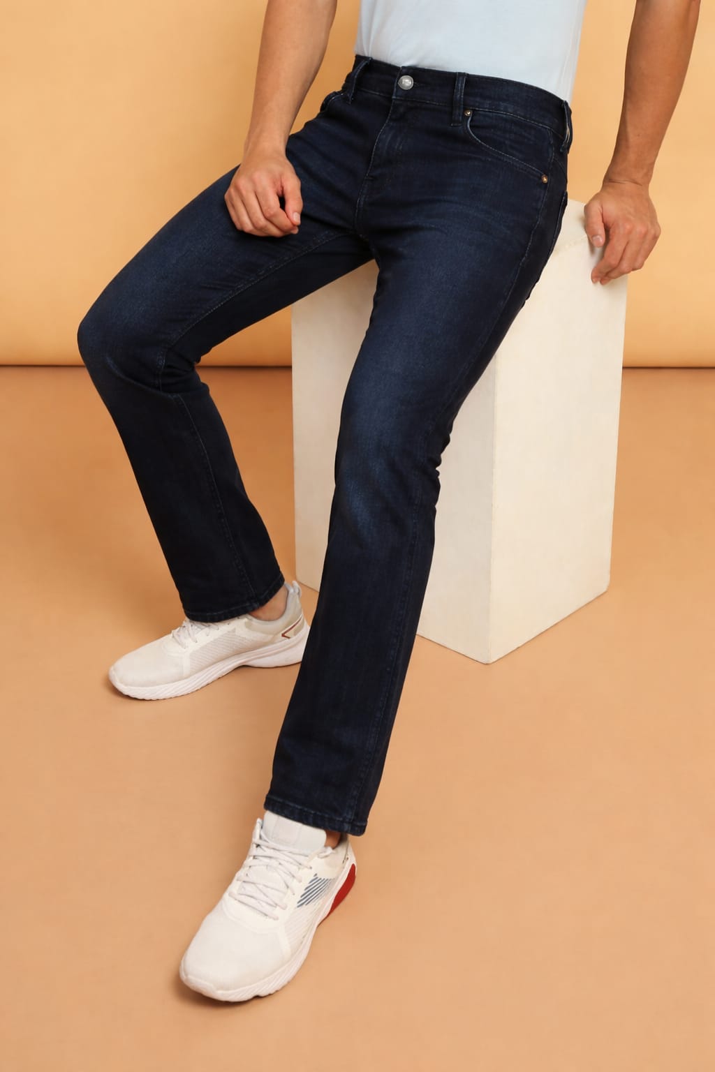 Person wearing dark blue jeans and white sneakers on a beige background