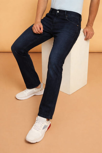 Person wearing dark blue jeans and white sneakers on a beige background
