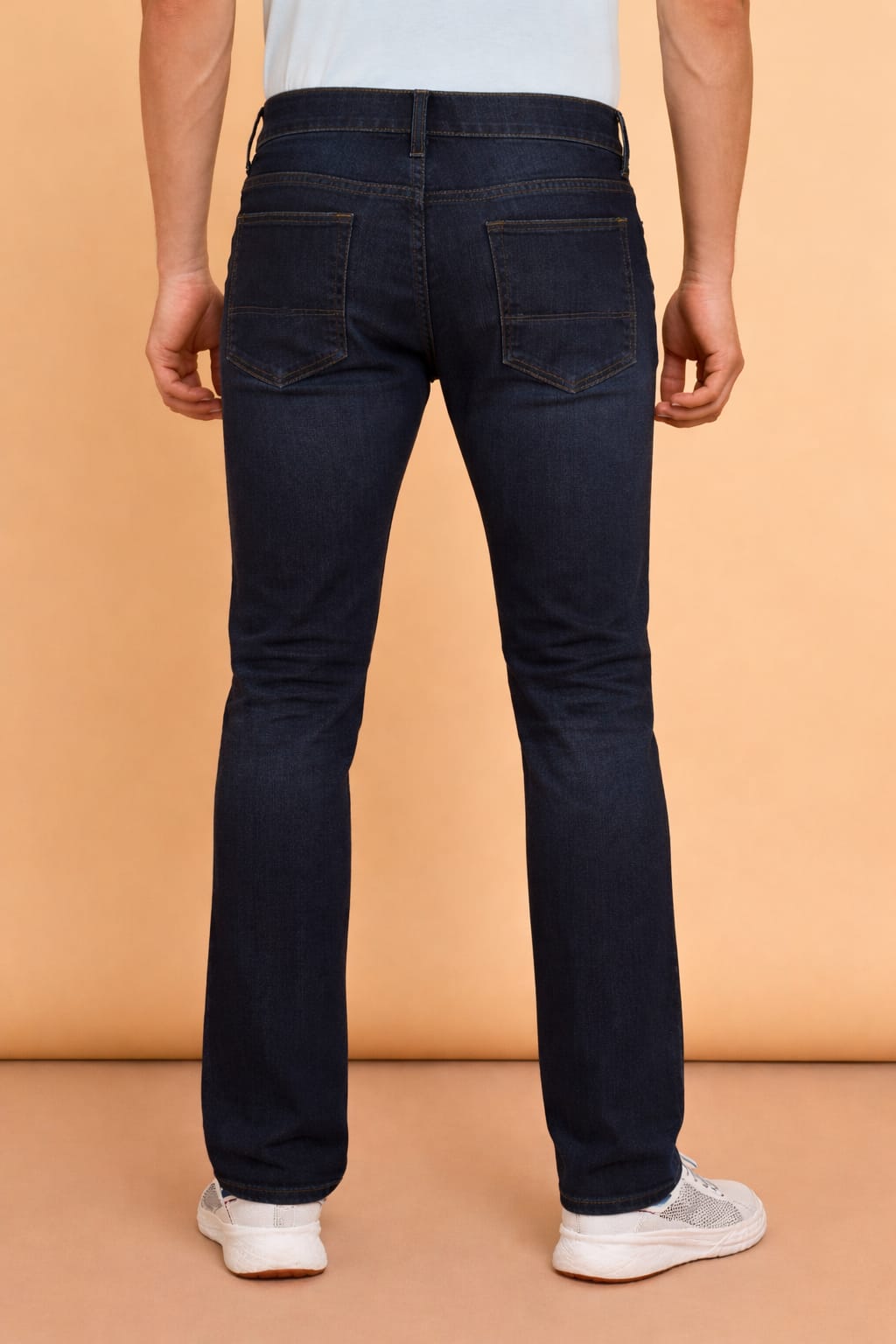 Person wearing dark blue jeans on a beige background