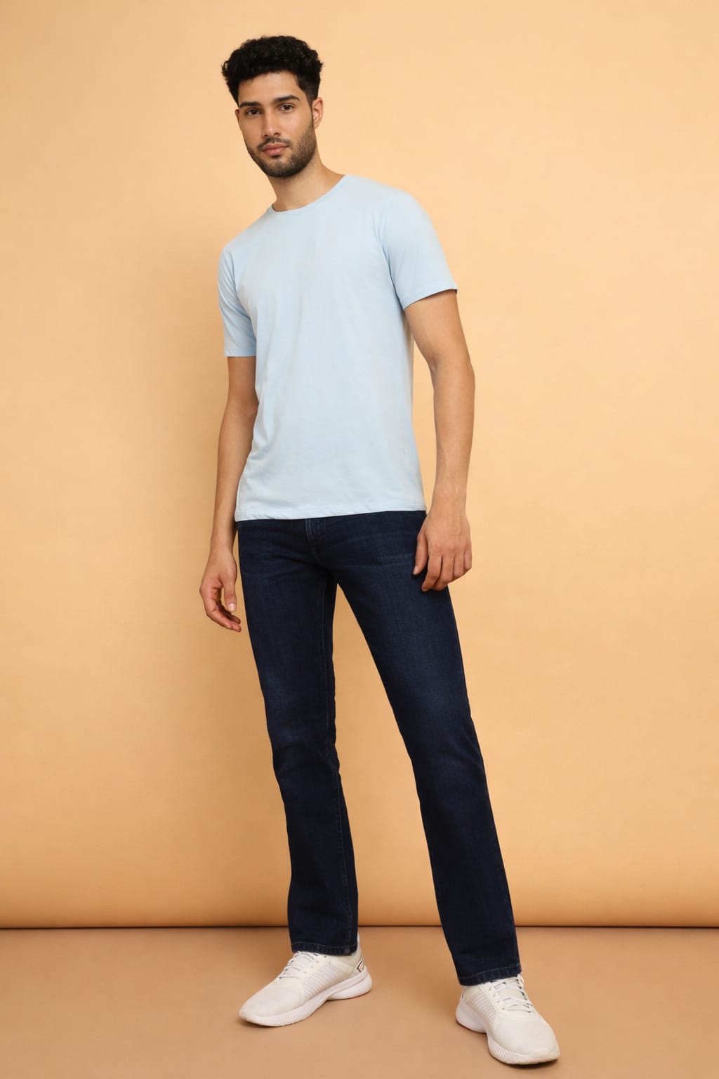 Man wearing a light blue t-shirt and dark jeans against a beige background