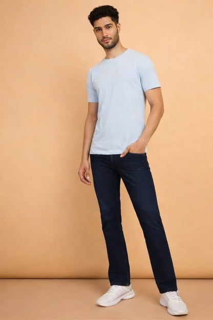 Man wearing a light blue t-shirt and dark jeans against a beige background