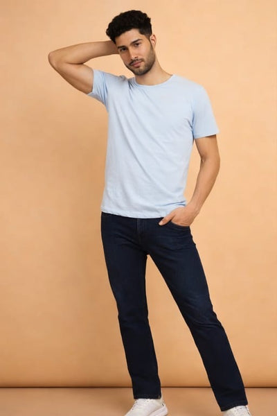 Man wearing a light blue t-shirt and dark jeans against a beige background