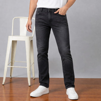 Person wearing black jeans and white sneakers standing on a wooden floor with a gray background.