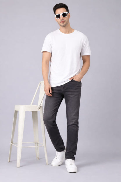 Man wearing a white t-shirt, dark jeans, and white sneakers on a gray background
