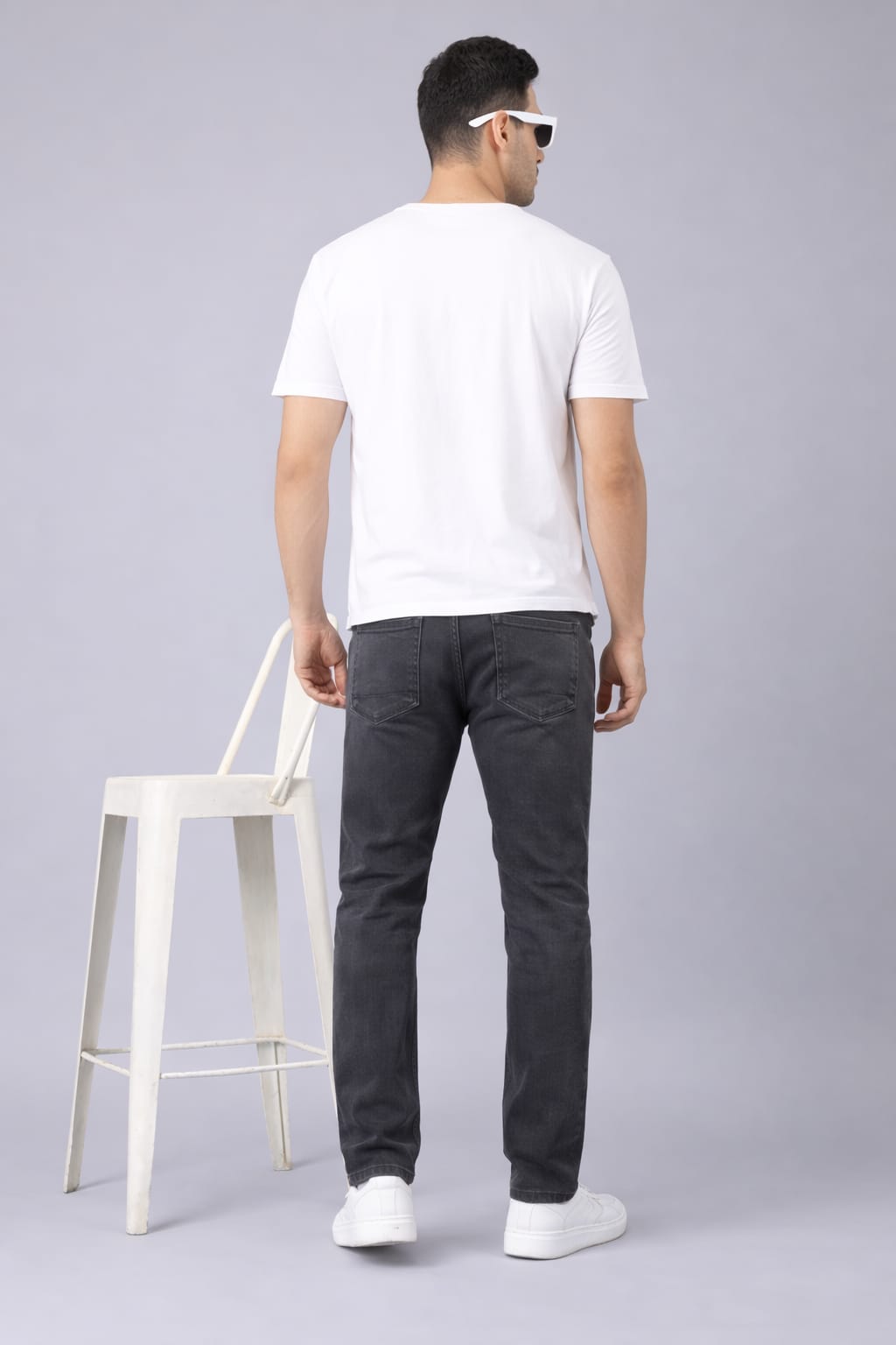 Man wearing a white t-shirt and dark jeans standing against a light gray background