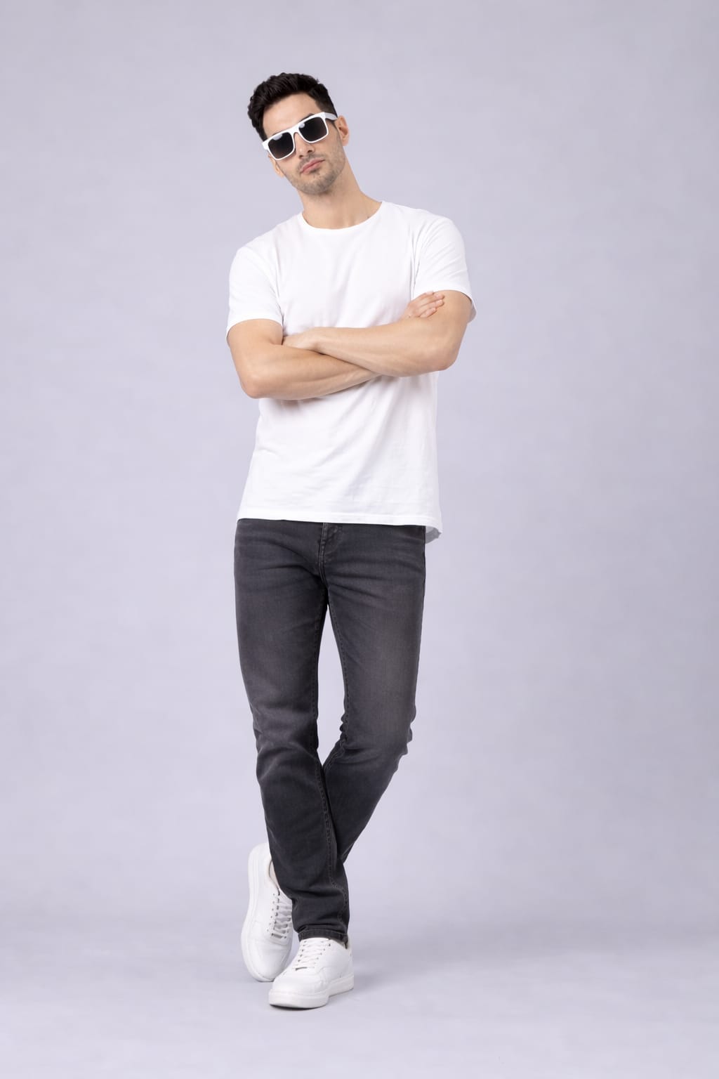 Man wearing a white t-shirt, dark jeans, and white sneakers on a light gray background
