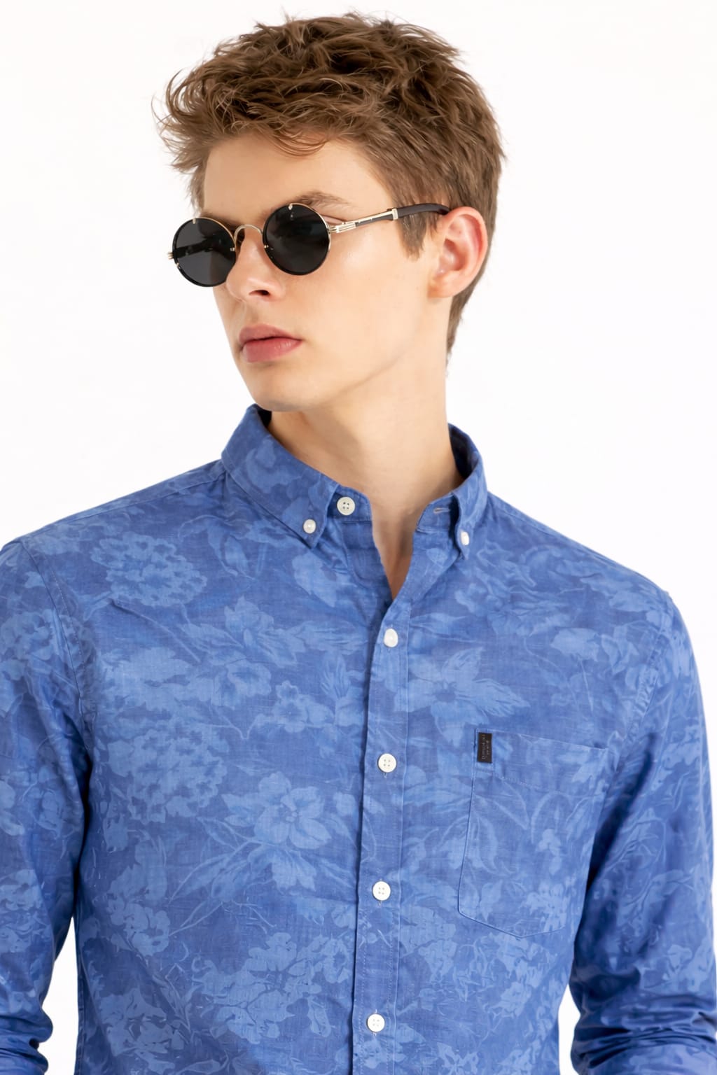 Man wearing a blue patterned shirt with sunglasses on a white background