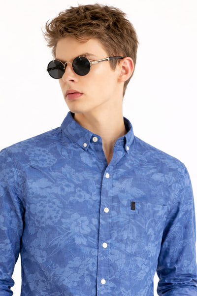 Man wearing a blue patterned shirt with sunglasses on a white background