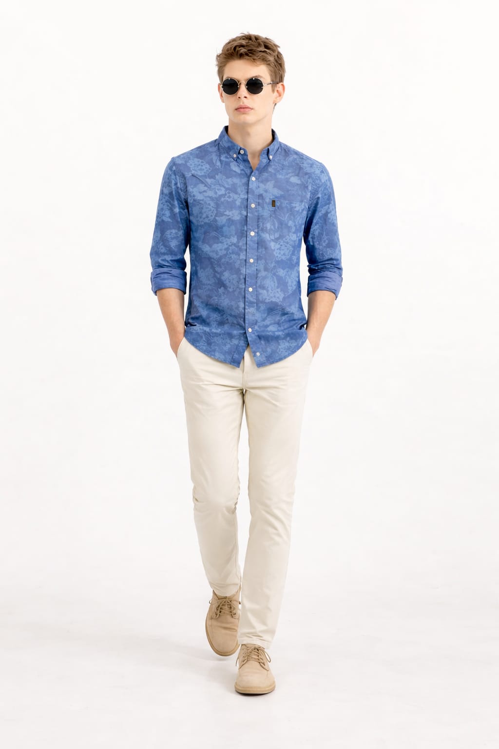 Man wearing a blue patterned shirt, beige pants, and sunglasses on a white background