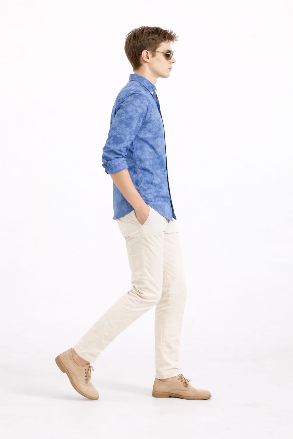 Man wearing a blue shirt, beige pants, and brown shoes on a white background