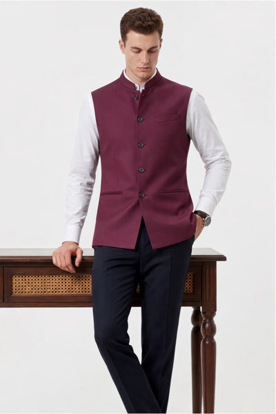 Man wearing a maroon vest over a white shirt with dark pants on a white background