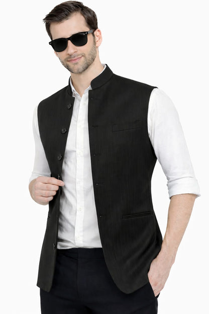 Man wearing a black vest over a white shirt with sunglasses on a white background